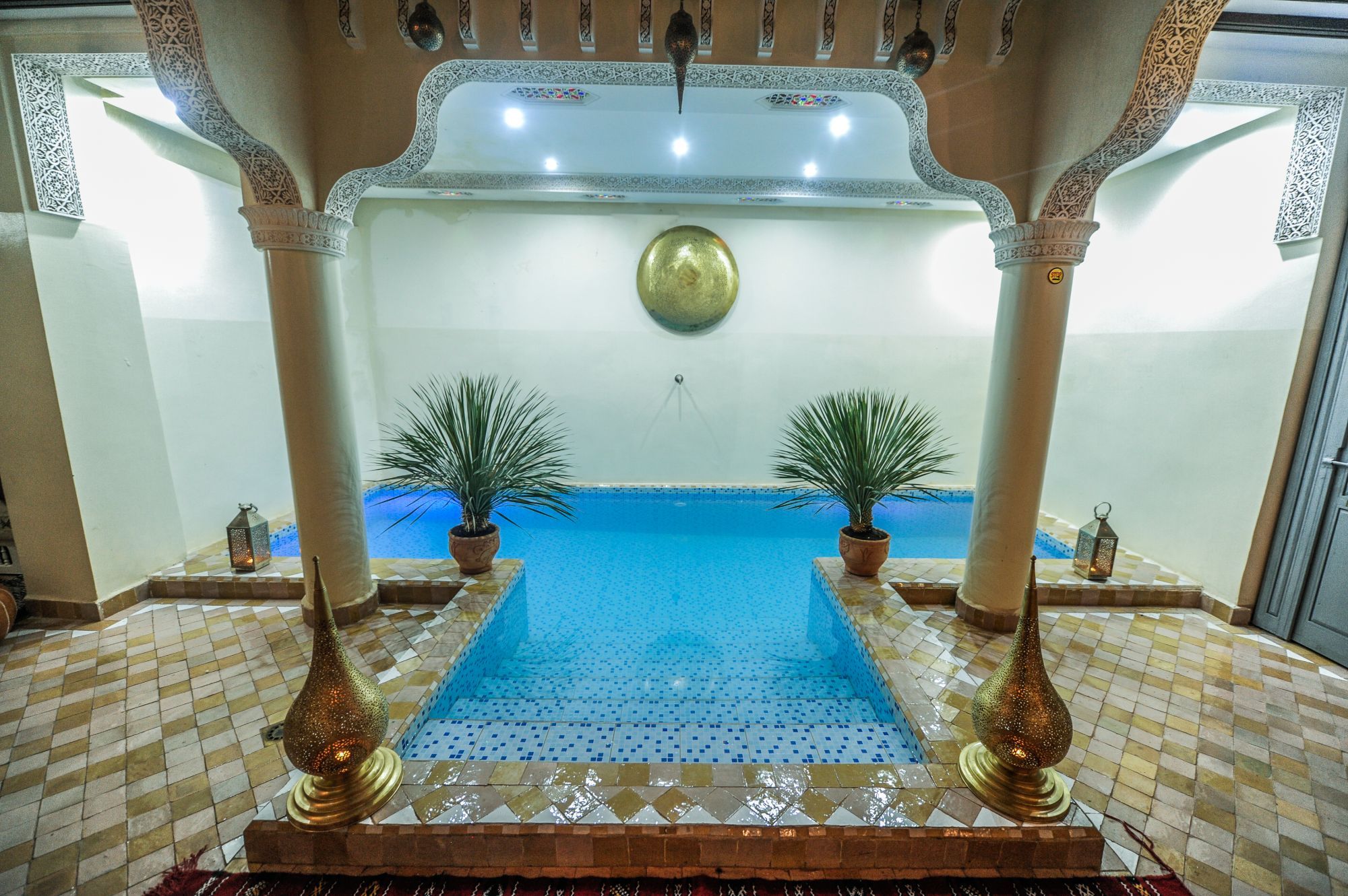 Innenhof des Riad Milouda mit türkisem Pool zwischen Säulen und Messinglaternen